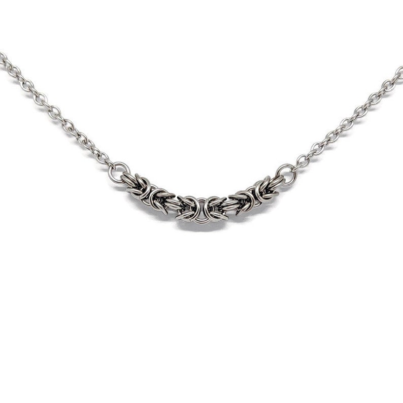 May include: A silver chain necklace with a woven design. The chain is made of small, interlocking links.