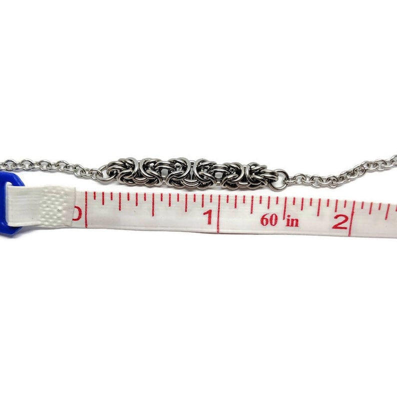 May include: A silver chain bracelet with a woven design, measured with a tape measure to be 1 1/2 inches long.