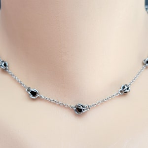 May include: A silver chain necklace with black metal beads. The necklace is on a white mannequin.