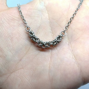 May include: A silver chain necklace with a woven design. The chain is made of small, interconnected metal rings.