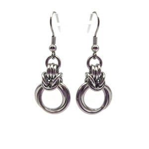 May include: A pair of silver-colored earrings. Each earring features a knotted design with multiple interlocking rings, suspended from a hook. The earrings are displayed against a white background, highlighting their metallic sheen and intricate craftsmanship.