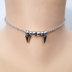 May include: A silver choker necklace with a row of round beads and two pointed spikes.
