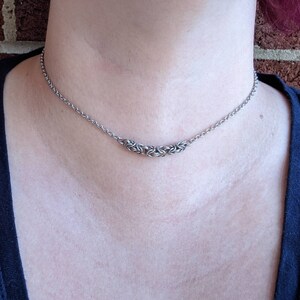 May include: A silver chain necklace with a small, intricate silver pendant. The pendant is made of multiple interwoven rings.