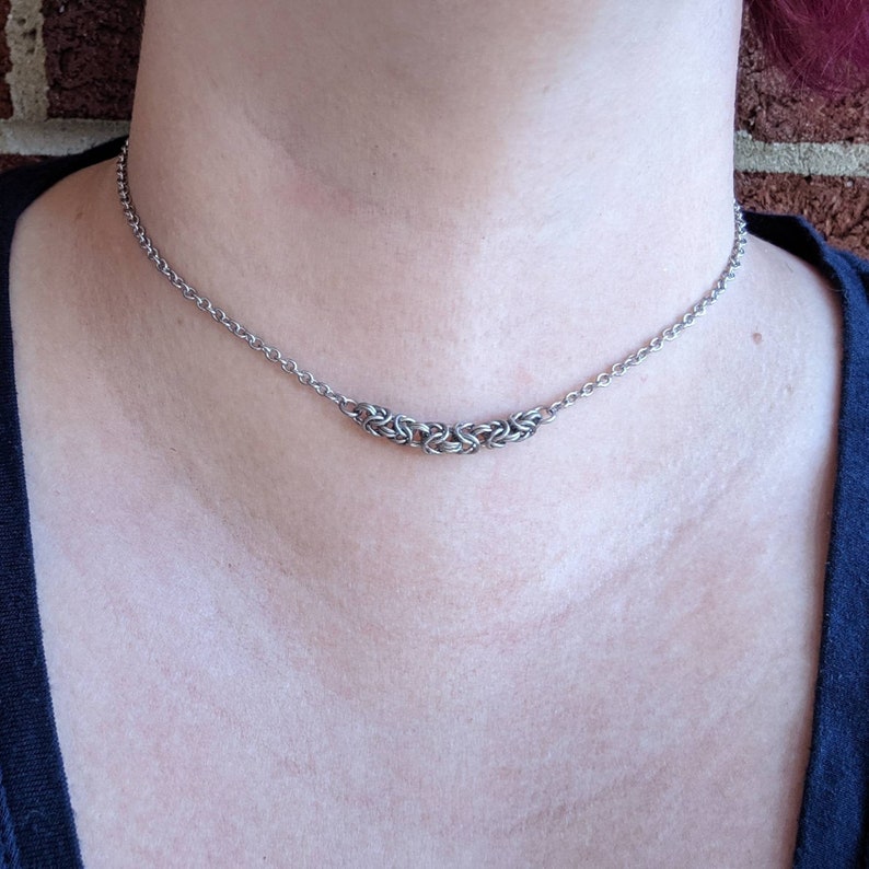 May include: A silver chain necklace with a small, intricate silver pendant. The pendant is made of multiple interwoven rings.