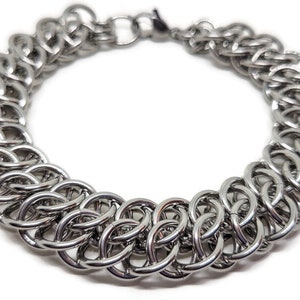 May include: A silver chain bracelet with a woven design. The bracelet is made of metal and has a polished finish.