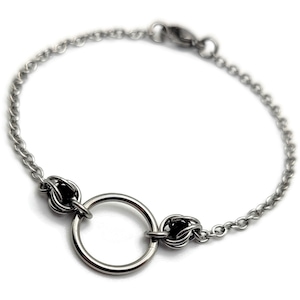 May include: A silver chain bracelet with a circular charm and two black bead accents.