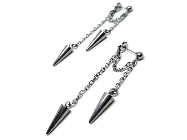 K&ouml;nnte beinhalten: Ein Paar silberne Ohrringe mit einer Kette und einem spitzen kegelf&ouml;rmigen Anh&auml;nger. Die Ohrringe sind f&uuml;r Knorpelpiercings konzipiert.