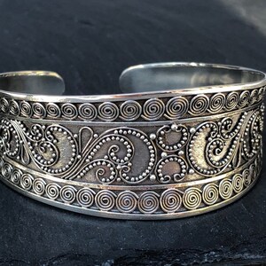 K&ouml;nnte beinhalten: Silberarmband mit aufwendigen floralen Designs und einer strukturierten Oberfl&auml;che.