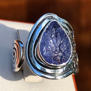 May include: A silver ring with a large, carved amethyst stone set in a swirling, organic design.