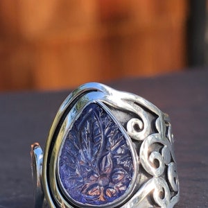May include: A silver ring with a teardrop-shaped purple stone set in a swirling, ornate design.