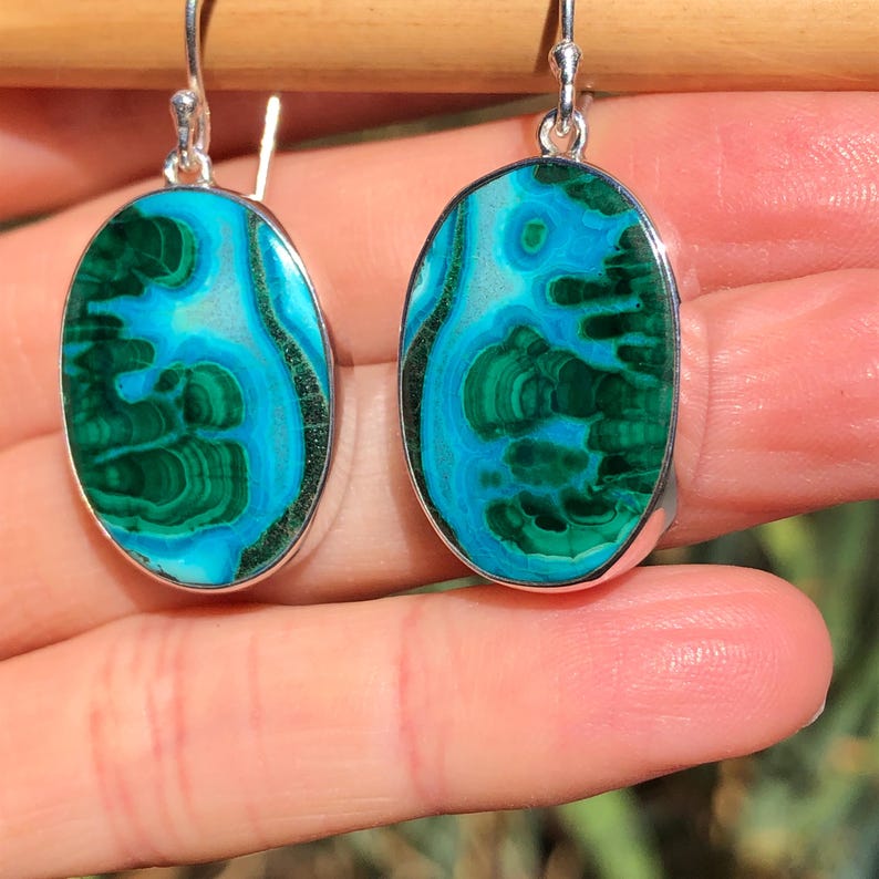 May include: A pair of oval-shaped earrings with green and blue malachite stones set in sterling silver.