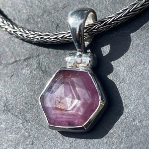 May include: A hexagonal faceted pink gemstone pendant set in a polished silver bezel with a hinged bail, suspended from a silver wheat chain. The stone displays natural inclusions and a translucent quality within its geometric silver frame.