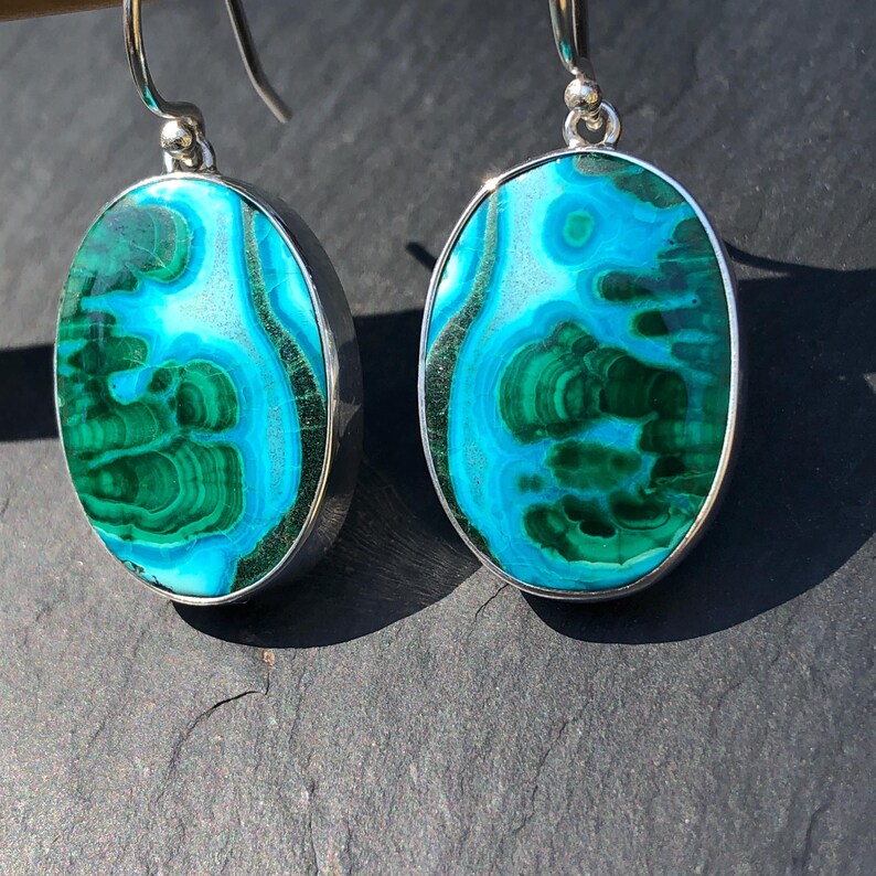 May include: A pair of silver earrings with oval-shaped turquoise and green gemstone stones. The stones have a swirling pattern of blue, green, and white.
