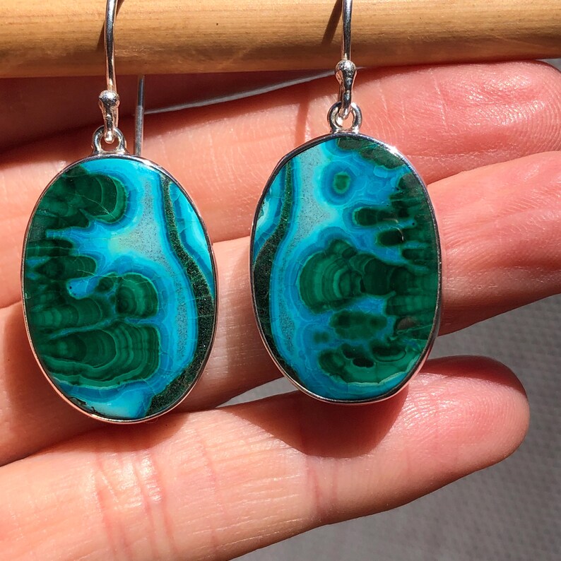 May include: A pair of oval-shaped earrings with a green and blue malachite stone set in sterling silver.