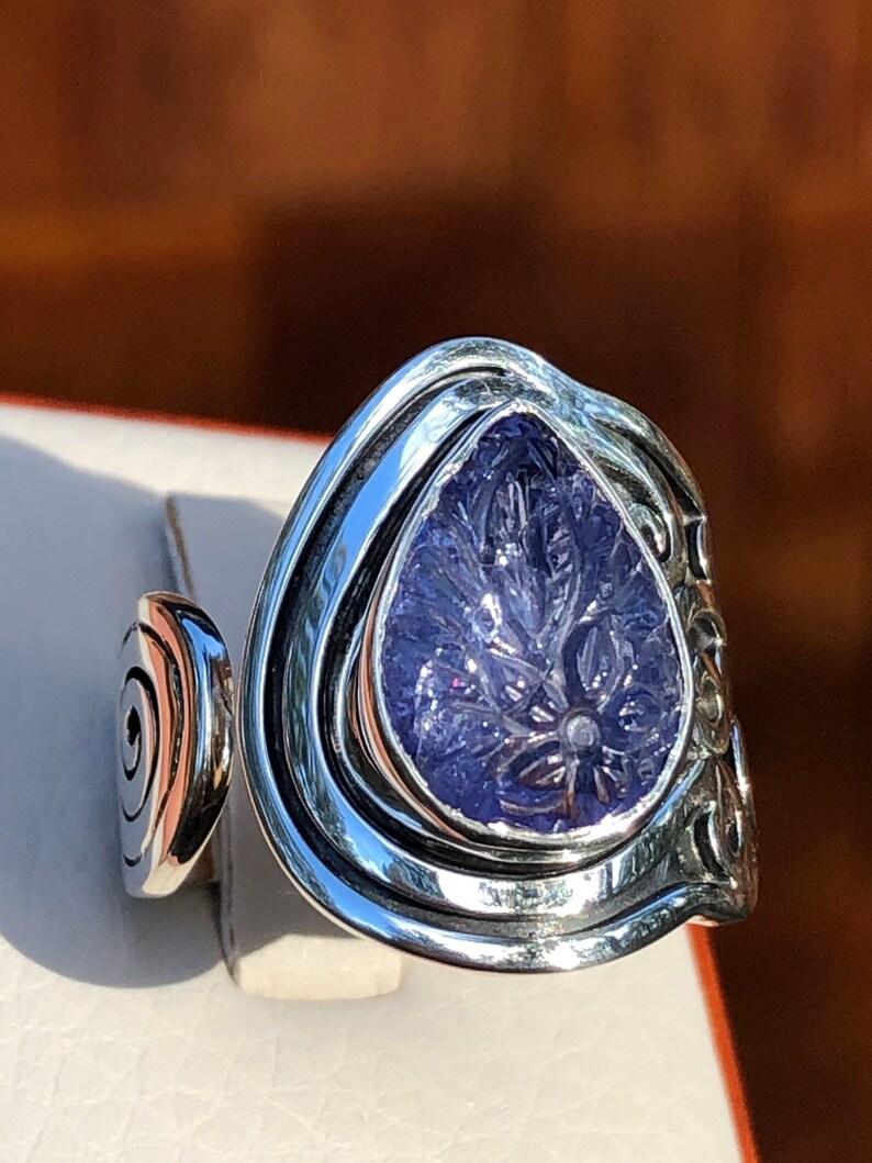 May include: A silver ring with a large, carved amethyst stone set in a swirling, organic design.