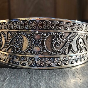 K&ouml;nnte beinhalten: Silberarmband mit aufwendigen floralen und spiralf&ouml;rmigen Designs. Das Armband ist breit und hat eine polierte Oberfl&auml;che.