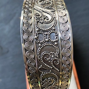 K&ouml;nnte beinhalten: Silberarmband mit komplizierten, wirbelnden Designs und einer strukturierten Oberfl&auml;che.
