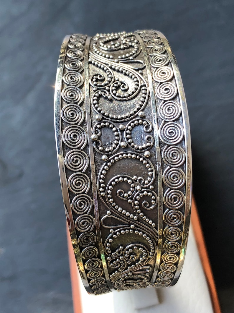K&ouml;nnte beinhalten: Silberarmband mit komplizierten, wirbelnden Designs und einer strukturierten Oberfl&auml;che.