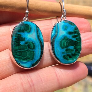May include: A pair of oval-shaped earrings with green and blue malachite stones set in sterling silver.