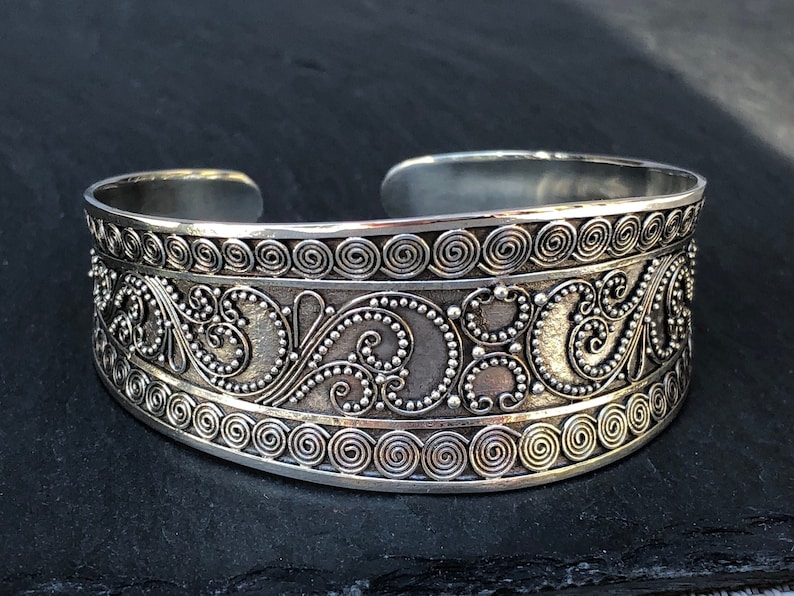 K&ouml;nnte beinhalten: Silberarmband mit aufwendigen floralen Designs und einer strukturierten Oberfl&auml;che.