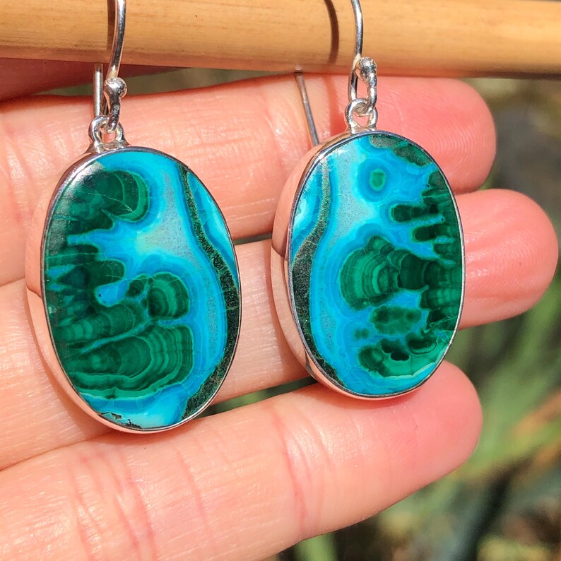 May include: A pair of oval-shaped earrings with green and blue malachite stones set in sterling silver.