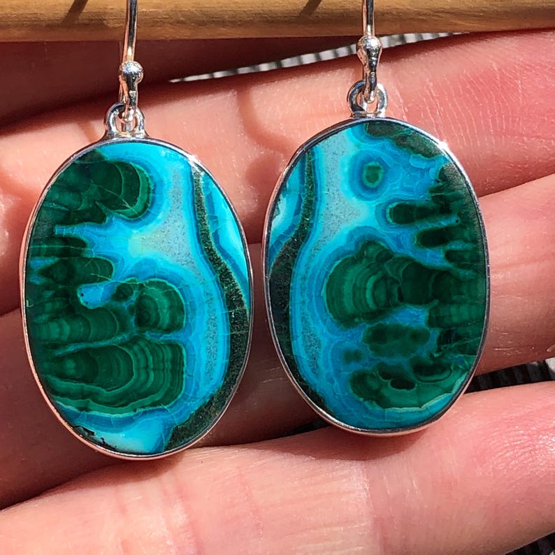May include: A pair of oval-shaped earrings with green and blue chrysocolla stones set in sterling silver.