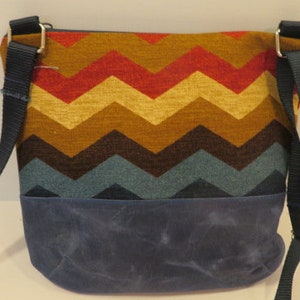 Crossbody bag has waxed canvas bottom and colorfull striped top. Zippered top.