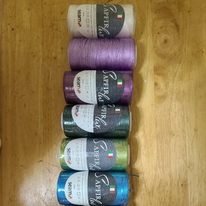 Puede incluir: Ocho carretes de hilo en varios colores, incluyendo blanco, morado, verde, azul, plateado y dorado. Cada carrete tiene el nombre de la marca "SAPFIR" impreso en &eacute;l, junto con el texto "LUCE" y una bandera italiana.