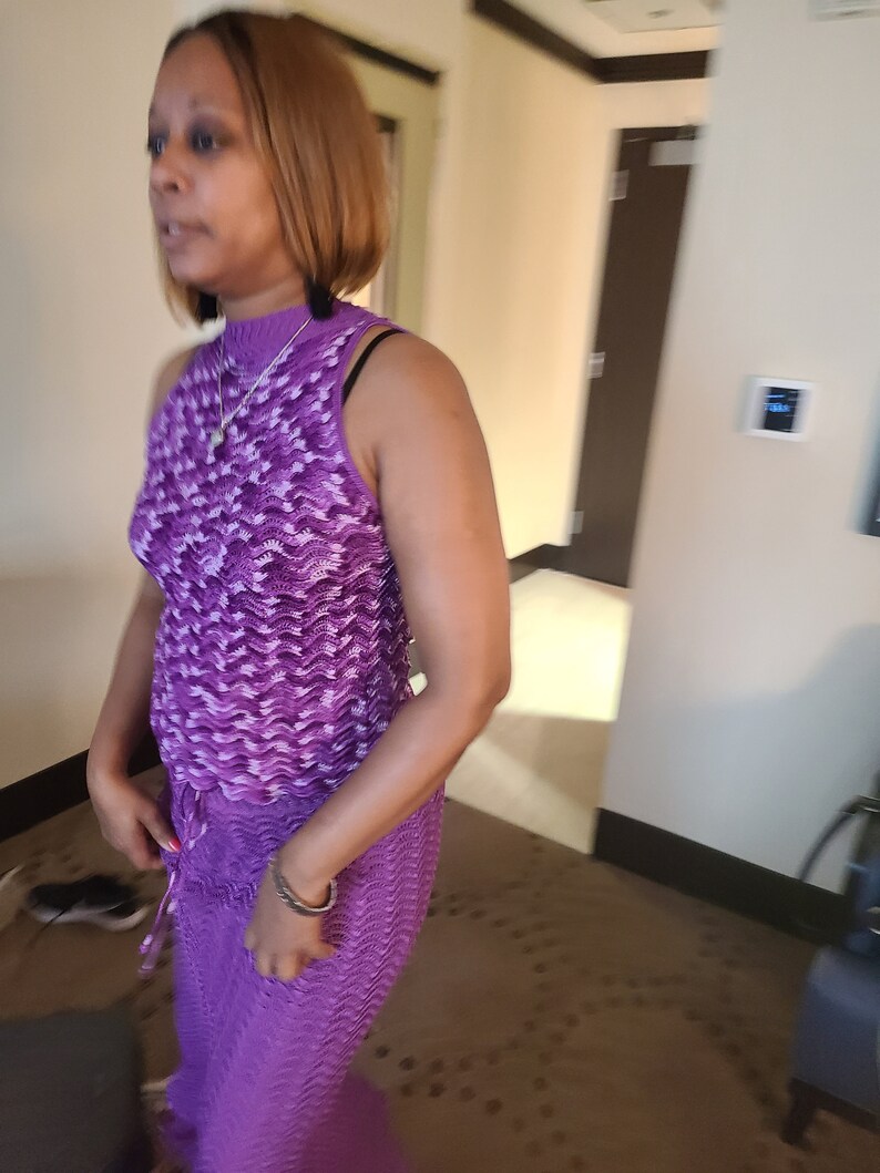 Puede incluir: Una mujer con un vestido sin mangas de color morado y blanco con cuello redondo. El vestido tiene un patr&oacute;n ondulado y una cintura con cord&oacute;n.