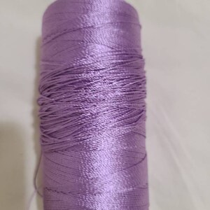 Puede incluir: Una bobina de hilo de color lavanda.