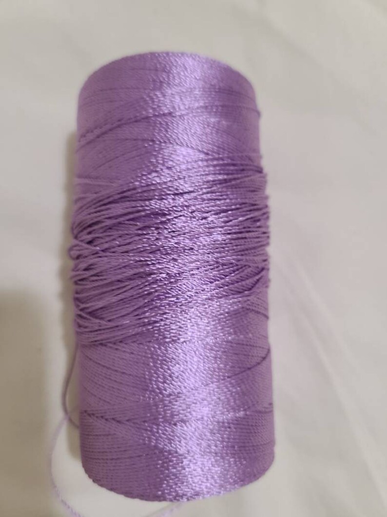 Puede incluir: Una bobina de hilo de color lavanda.