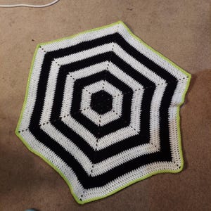 May include: A black and white crocheted hexagon blanket with a lime green border.