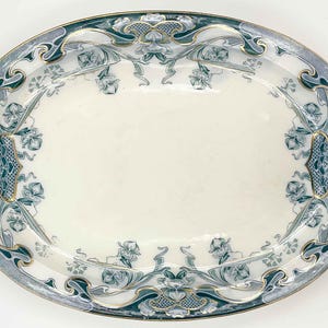 May include: An oval ceramic serving platter featuring a cream-colored center and a wide, decorative border. The border displays intricate teal and blue floral patterns with flowing, organic lines and delicate gold-toned trim along the edges.