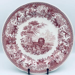 Peut inclure: Une assiette ronde en céramique ornée d'un motif de transfert marron foncé sur fond blanc. Le centre représente un lion dans un paysage, tandis que la large bordure est décorée de motifs floraux complexes et de feuillages en volutes.