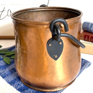May include: A copper bucket with a black handle and a decorative black plate. The bucket is on a blue and white striped cloth. The words "wherever we are" are in the background.
