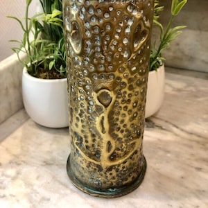 May include: A brass vase with a hammered texture and a design of hearts. The vase is about 10 inches tall and has a diameter of about 4 inches.