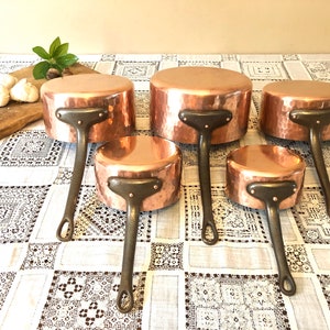 May include: Set of five copper saucepans with hammered surfaces and dark brown handles.