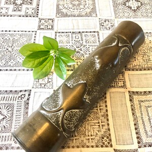 May include: A vintage brass vase with a textured surface and a floral design. The vase is cylindrical and has a slightly rounded bottom.