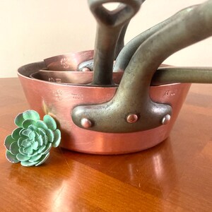 May include: Set of four copper saucepans with long handles. The saucepans are nested together and have a vintage look. The largest saucepan has the text "Villeroy & Boch" stamped on the bottom.