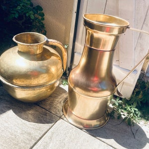 May include: Two antique brass pitchers, one with a round body and a short spout, the other with a tall, slender body and a long spout. Both pitchers have a handle.