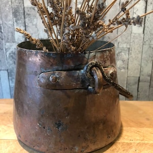 May include: A vintage copper pot with a handle and a worn patina. The pot is filled with dried lavender.