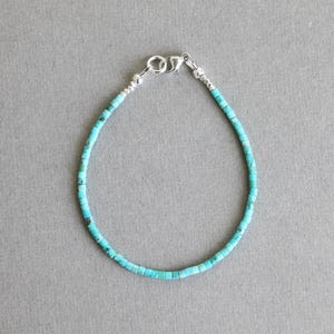 May include: A delicate turquoise beaded bracelet with a silver clasp. The bracelet is made of small, square-shaped beads in varying shades of blue-green. The clasp is a simple, secure design.