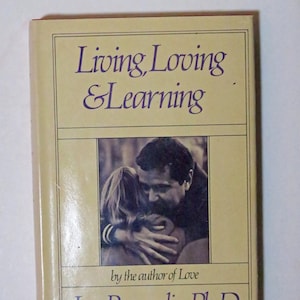 May include: A yellow book cover with the title "Living, Loving & Learning" by the author of Love, Leo Buscaglia, Ph.D. The cover features a black and white photograph of a couple embracing.