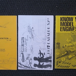 May include: Three vintage aviation publications are displayed. The yellow cover on the left reads "Cirrus Aviation Ltd." with aircraft illustrations. The center catalog is titled "Oldtimer Model Supply." The right book is titled "Know Your Model Aero Engines."