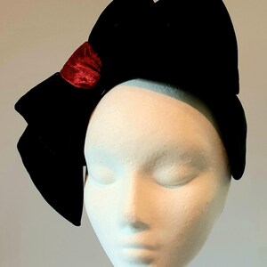 以下が含まれることがあります： 黒いベルベットのリボンヘアバンドと小さな赤いベルベットのアクセント。リボンは大きく、白いマネキンの頭の上にあります。ヘアバンドはファッションアクセサリーです。