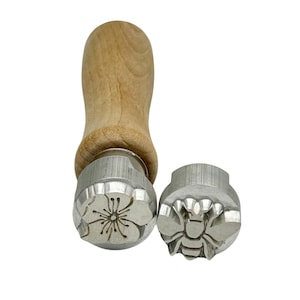May include: Two metal cookie stamps with wooden handles. One stamp features a flower design and the other a bee design.