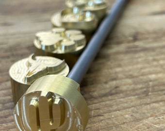 May include: Five brass branding irons with different designs, including a cactus, a bull's head, a flower, and two other designs. The irons are attached to a long metal rod.