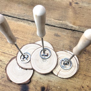 Op de afbeelding: Drie brandingijzers met houten handvatten en metalen punten in de vorm van de letters R, L en E. De ijzers worden gepresenteerd op drie houten rondjes.