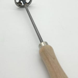 Op de afbeelding: Een metalen brandmerk met een houten handvat. Het brandmerk heeft een ronde kop met de letter "R" uitgesneden.