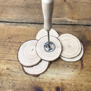 Op de afbeelding: Een set van vier houten onderzetters met een metalen brandmerk in het midden. De onderzetters zijn gemaakt van natuurlijk hout met een lichtbruine kleur en hebben een ronde vorm. Het brandmerk is een eenvoudig ontwerp met een enkele letter "T" in het midden.